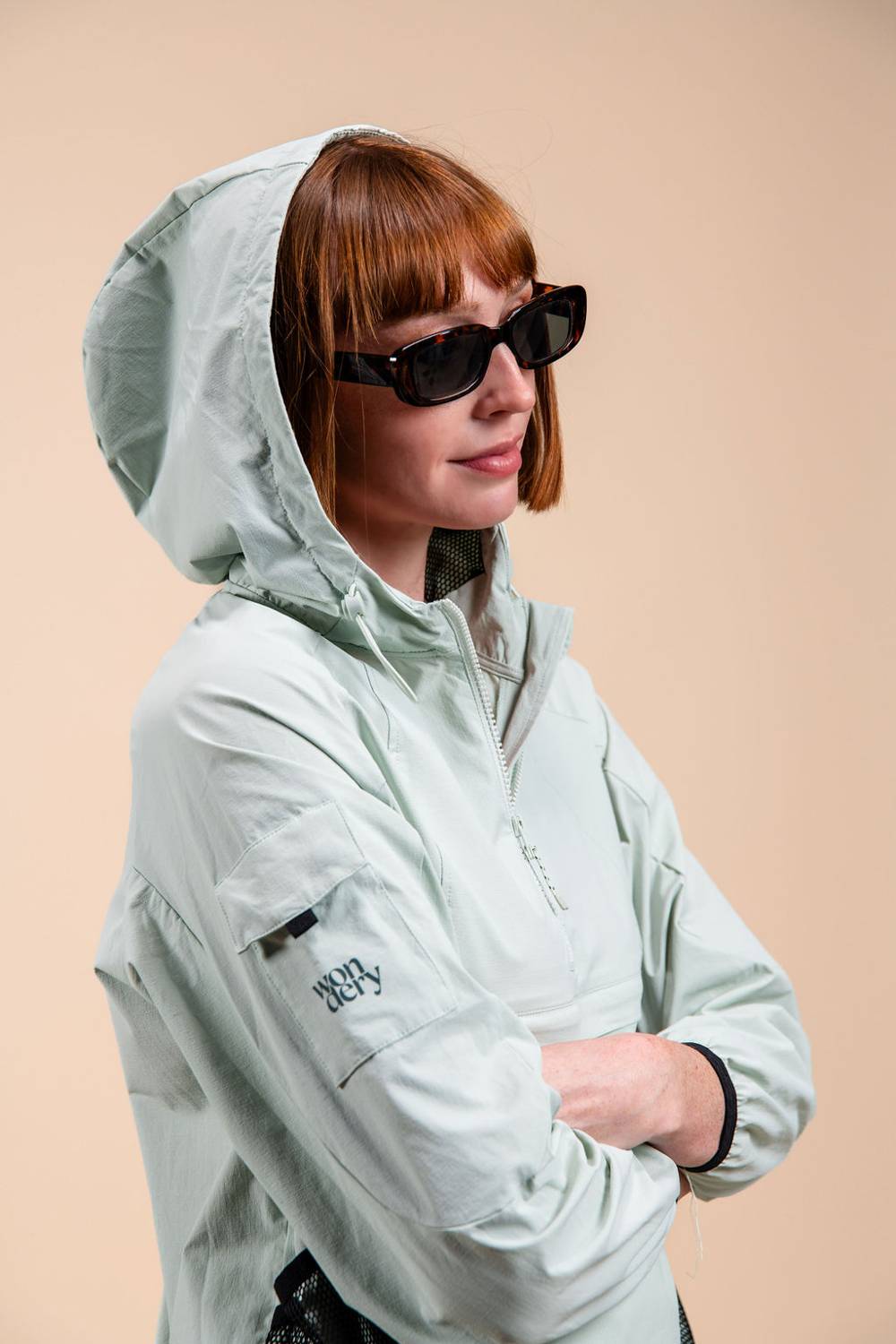 Red head woman with tortoise pattern sunglasses and lightweight green jacket hood over head