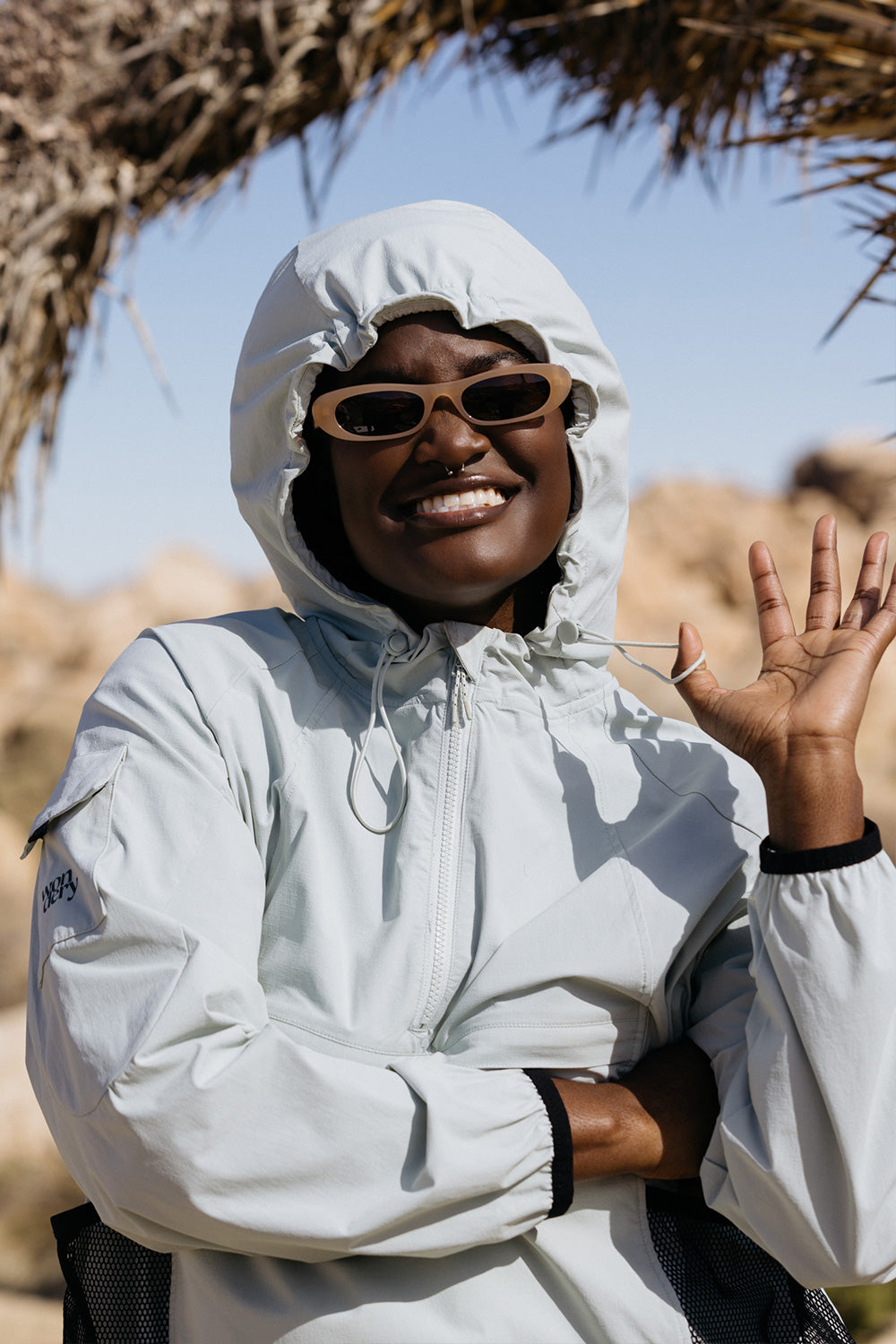 black woman in desert wearing lightweight jacket and oval sunglasses with hood over head